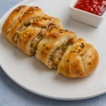 Freshly baked braided chicken bread filled with savory shredded chicken and vegetables, sliced on a white plate.