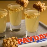 Glasses of Payday Shot Drink garnished with crushed peanuts and a chunk of Payday candy bar.
