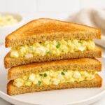 Triangular egg salad sandwiches stacked on a white plate, made with the classic Augusta Masters egg salad recipe