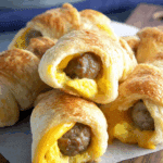 Golden brown sausage egg and cheese breakfast roll-ups with melted cheese and flaky pastry.