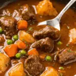 A hearty bowl of Beef Stew with chunks of beef, potatoes, carrots, and peas in a rich brown broth.