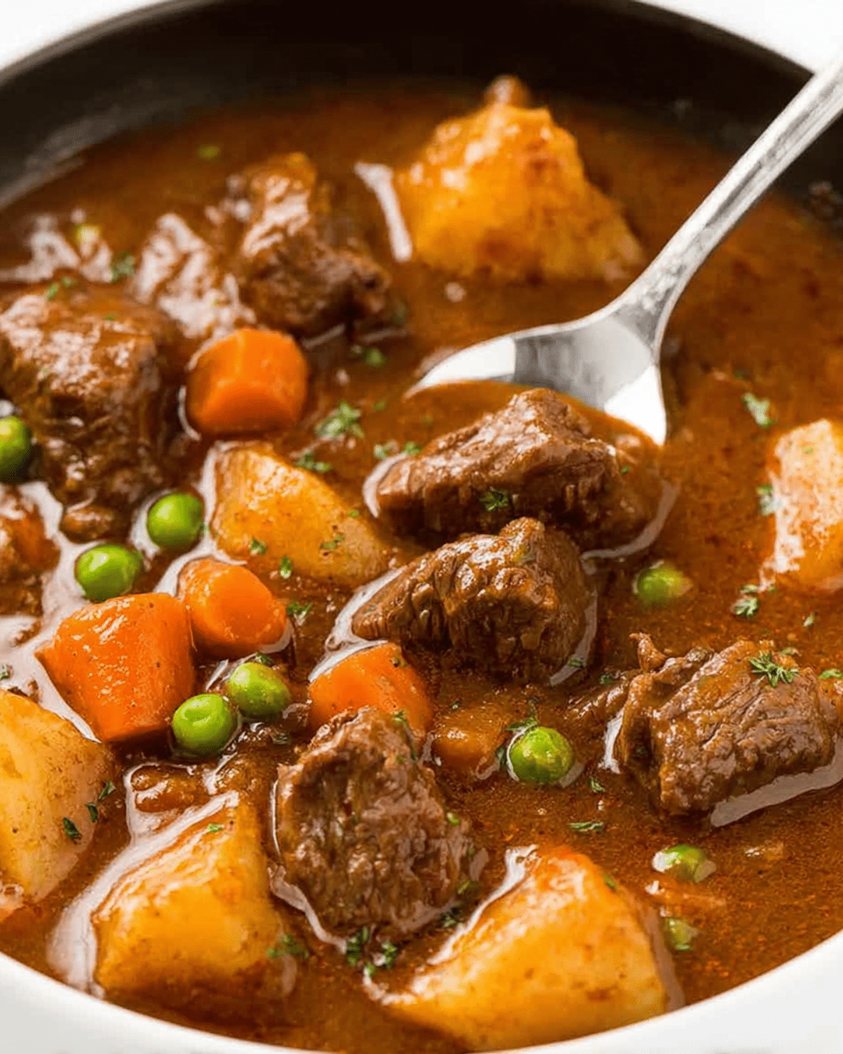 A hearty bowl of Beef Stew with chunks of beef, potatoes, carrots, and peas in a rich brown broth.