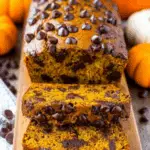 Sliced loaf of the best chocolate chip pumpkin bread, loaded with melty chocolate chips and surrounded by mini pumpkins.