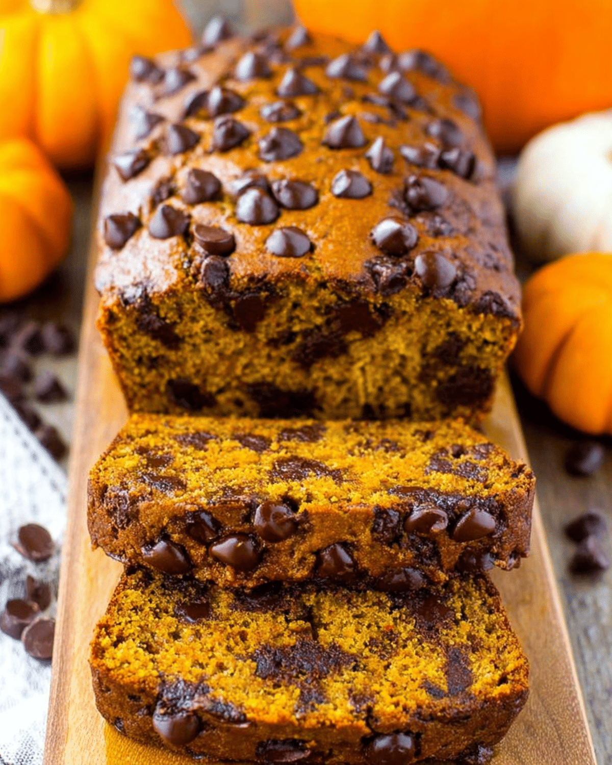 Sliced loaf of the best chocolate chip pumpkin bread, loaded with melty chocolate chips and surrounded by mini pumpkins.