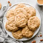 Chewy Maple Brown Sugar Cookies drizzled with maple glaze, stacked on a white plate with pecan pieces.
