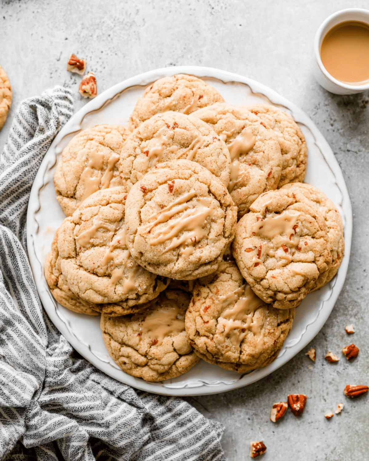 Chewy Maple Brown Sugar Cookies drizzled with maple glaze, stacked on a white plate with pecan pieces.