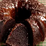 Chocolate zucchini bundt cake topped with chocolate glaze and mini chocolate chips, with a slice cut.
