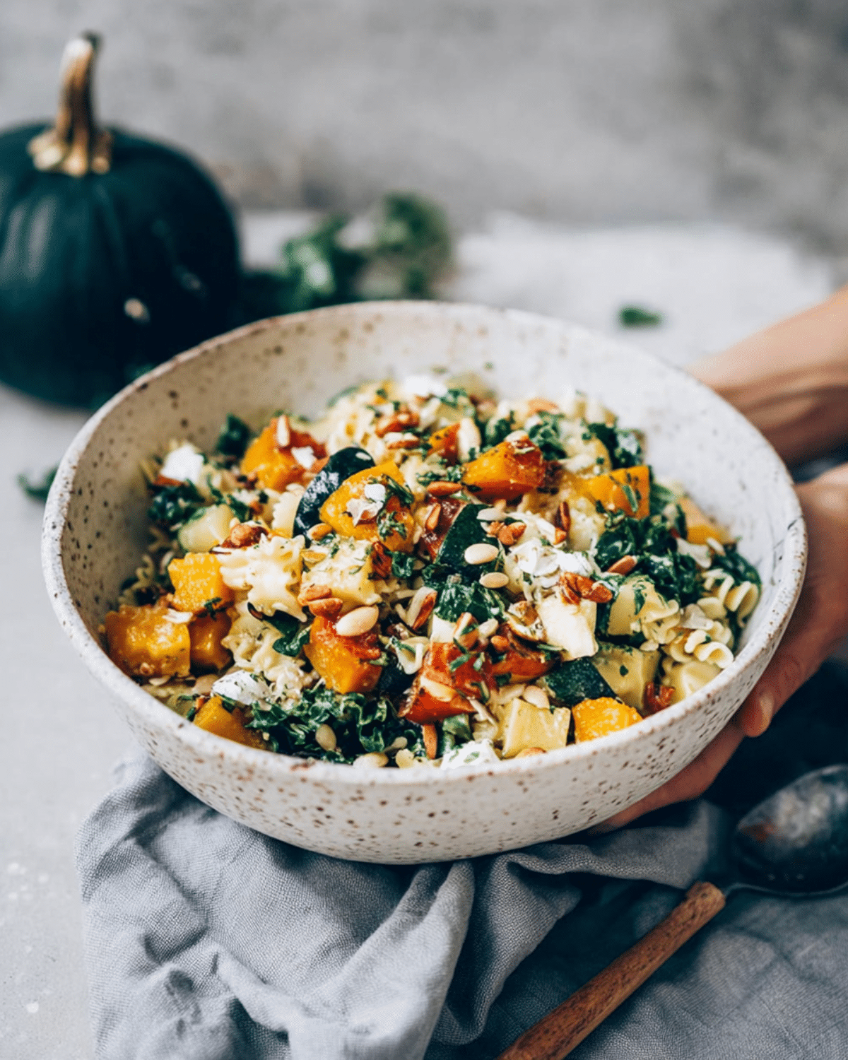 Cold Fall Pasta Salad with Squash and Kale in a speckled ceramic bowl, featuring rotini pasta, roasted squash, kale, seeds, and herbs.