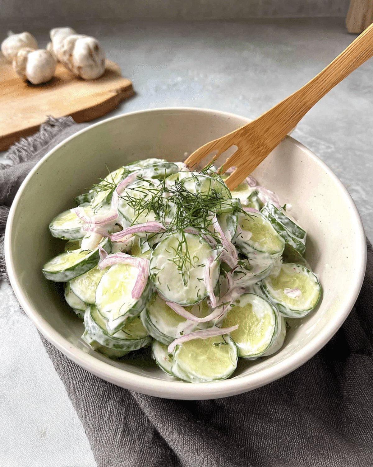 Bowl of creamy cucumber salad with sliced cucumbers, red onions, fresh dill, and a creamy dressing, served with a wooden fork.
