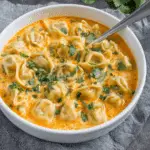 Creamy Thai Dumpling Soup in a white bowl, garnished with fresh cilantro and filled with plump dumplings in a rich, orange-hued broth.
