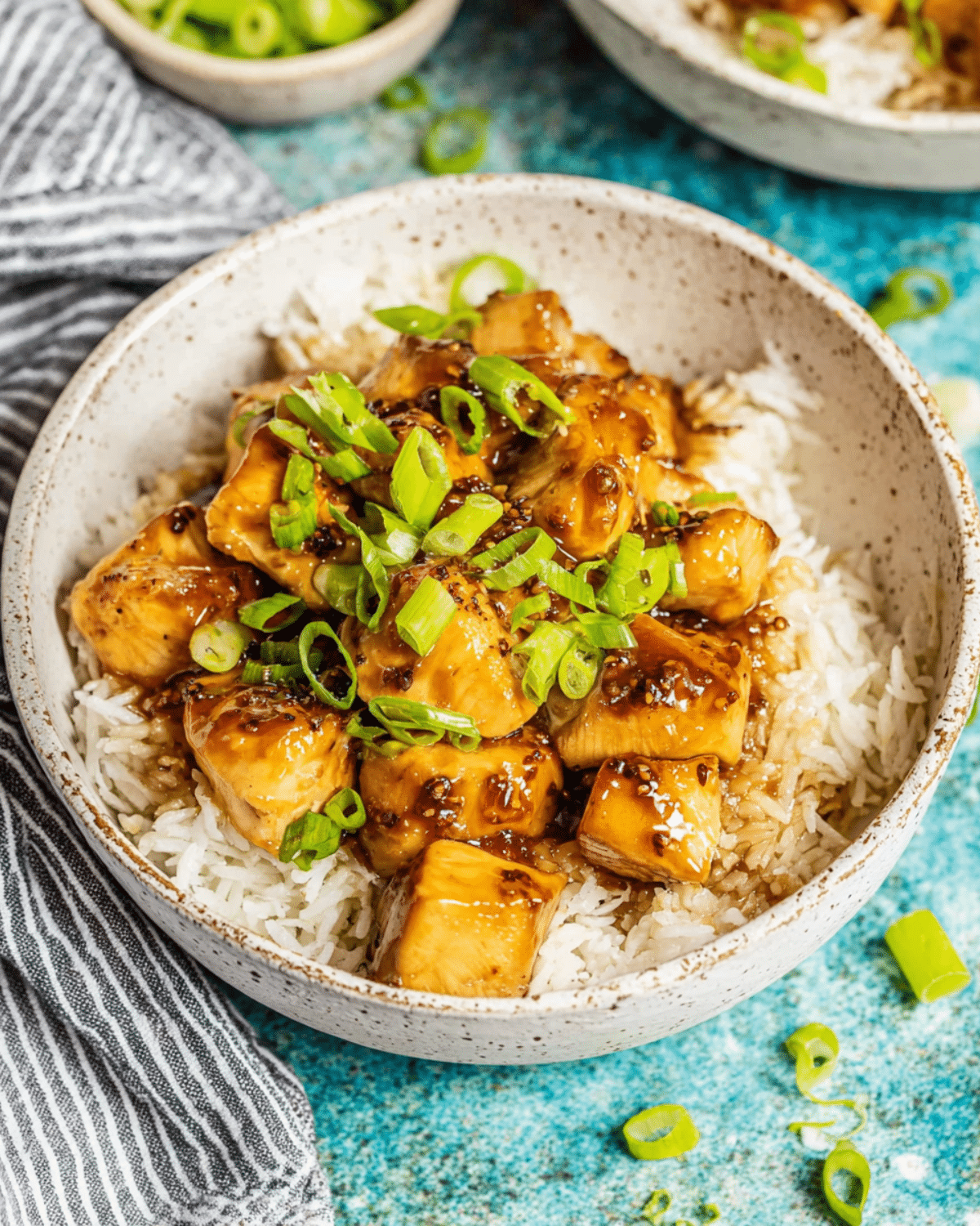 A bowl of crock pot bourbon chicken served over white rice and topped with chopped green onions.