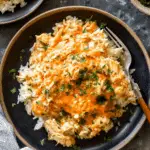 A plate of crock pot chicken and rice topped with shredded chicken in a creamy orange sauce and garnished with chopped parsley.