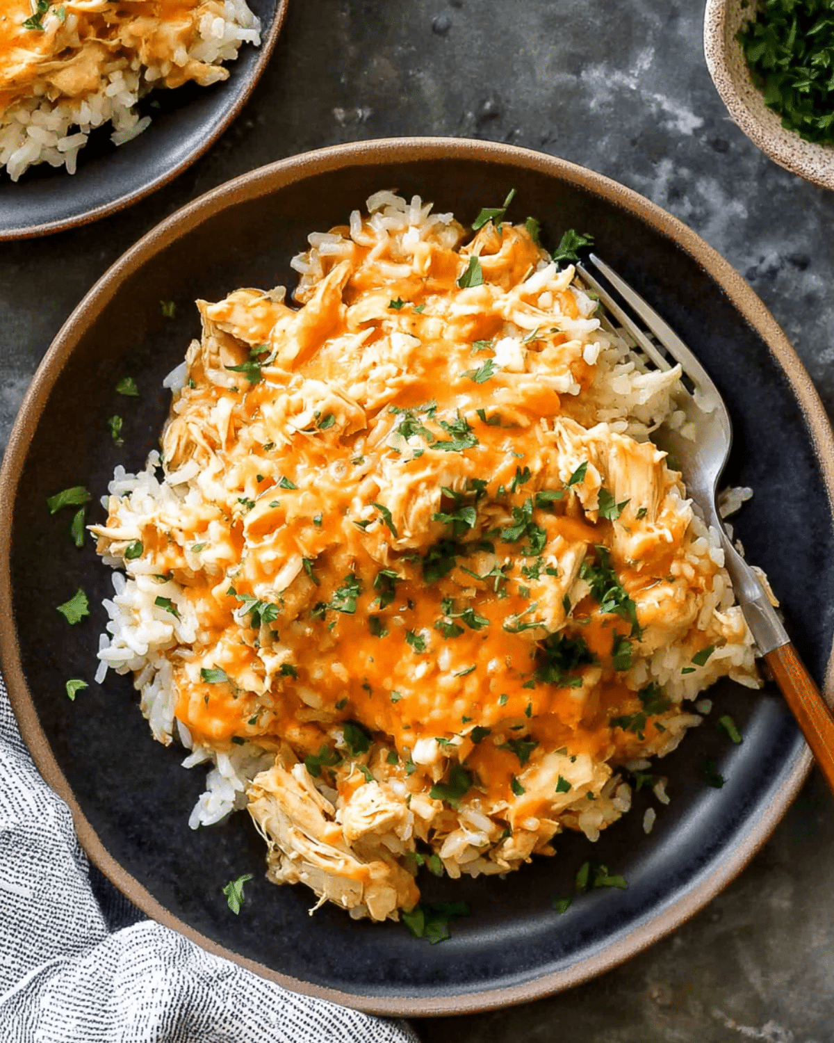 A plate of crock pot chicken and rice topped with shredded chicken in a creamy orange sauce and garnished with chopped parsley.