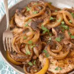 A bowl of crock pot pork chops topped with caramelized onions and garnished with fresh parsley.