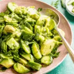 Bowl of cucumber avocado salad with chopped herbs and a spoon on the side.