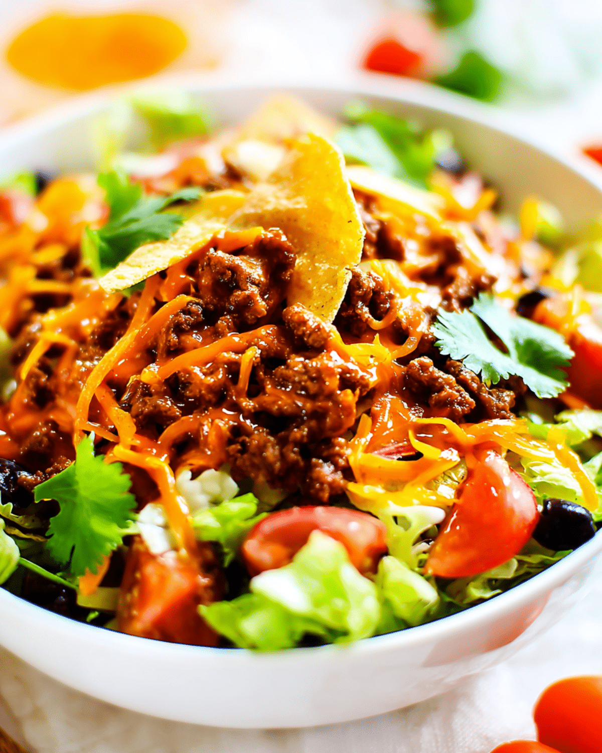 A colorful Doritos Taco Salad in a white bowl, topped with seasoned ground beef, shredded cheese, fresh vegetables, and crushed Doritos chips.