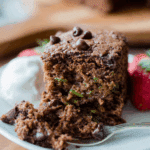 Slice of double chocolate zucchini cake with chocolate chips and shredded zucchini, served with whipped cream and strawberries.
