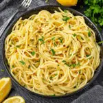 Easy Lemon Butter Garlic Pasta topped with fresh parsley and red pepper flakes, served in a black bowl with lemon wedges on the side.