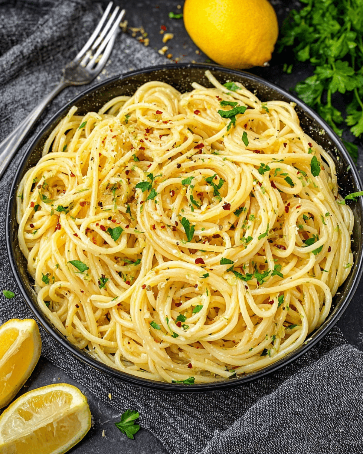 Easy Lemon Butter Garlic Pasta topped with fresh parsley and red pepper flakes, served in a black bowl with lemon wedges on the side.