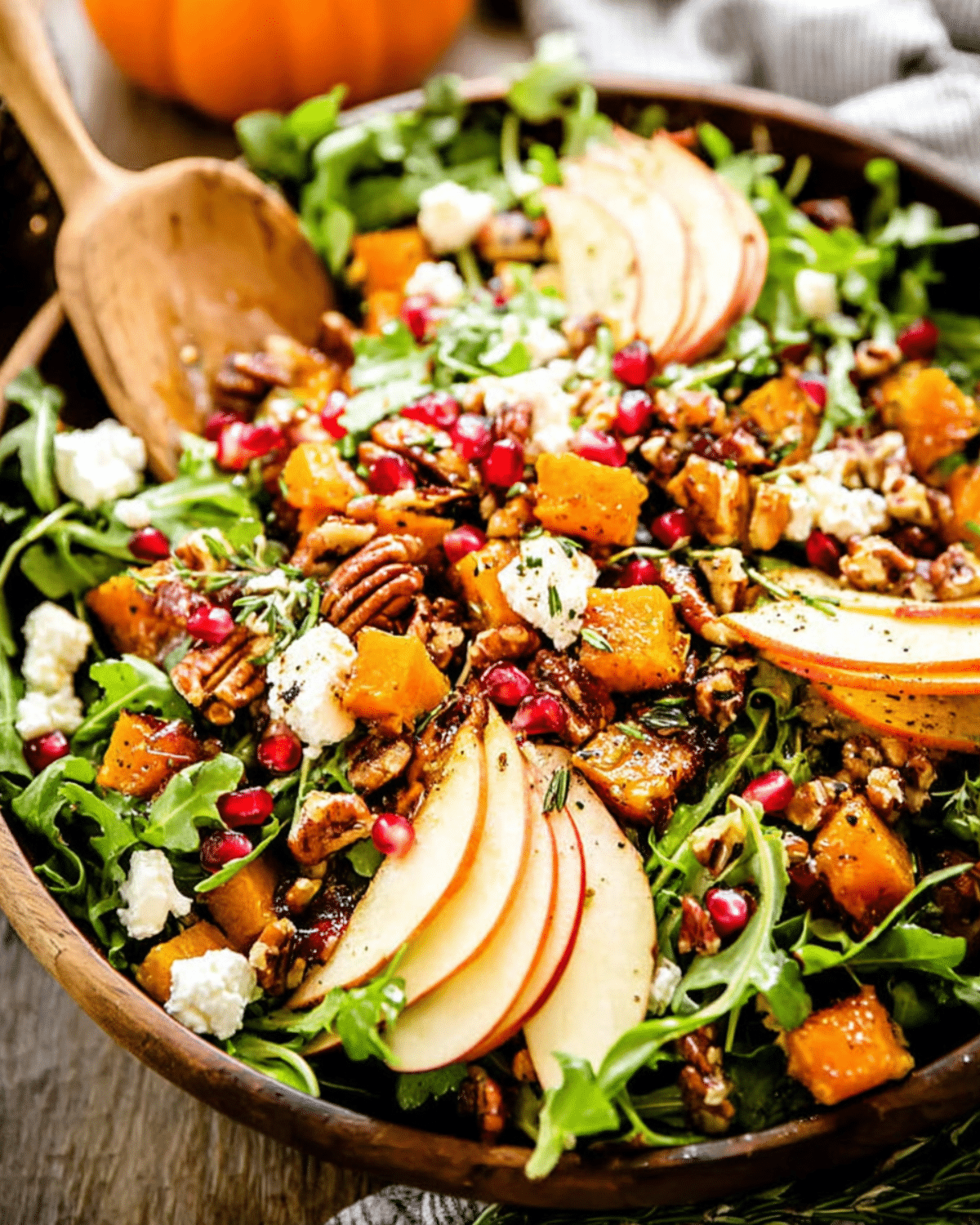 Fall Harvest Salad with roasted butternut squash, apple slices, pecans, goat cheese, pomegranate seeds, and arugula in a wooden bowl.