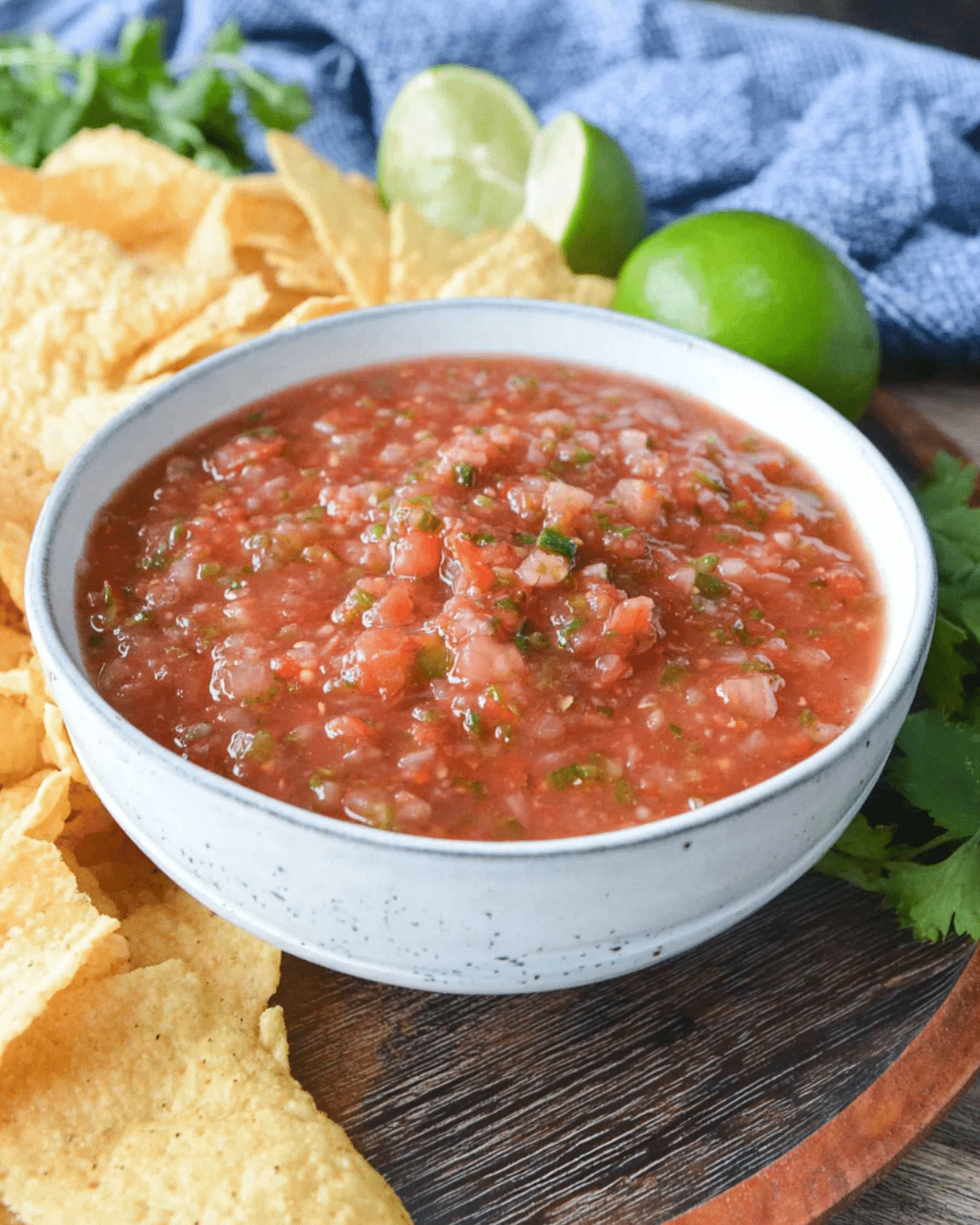 Bowl of fire roasted salsa surrounded by tortilla chips, limes, and fresh cilantro.