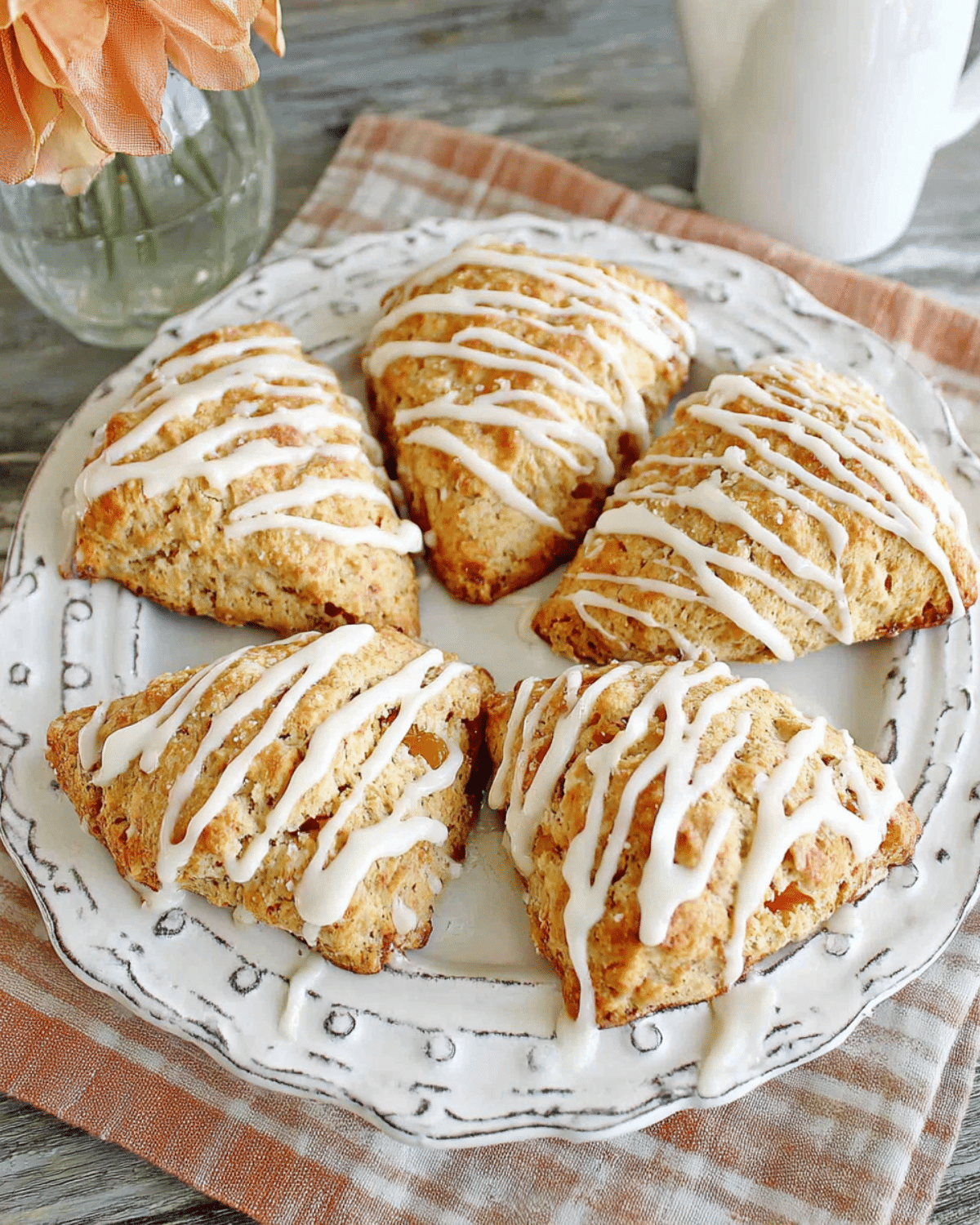 A plate of golden Flaky Apricot Scones drizzled with white icing, arranged neatly on a decorative dish with a soft plaid napkin underneath.