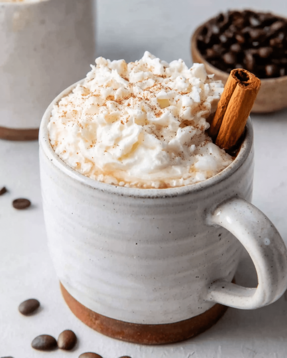 A rustic ceramic mug filled with maple cinnamon latte, topped with whipped cream, sprinkled with cinnamon, and garnished with a cinnamon stick.