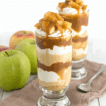 No bake caramel apple pie cheesecake parfaits layered with whipped cream, caramel, and apple topping in tall glasses.