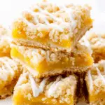Peach Bars stacked on a white plate, featuring a crumbly topping, sweet peach filling, and a drizzle of white icing.
