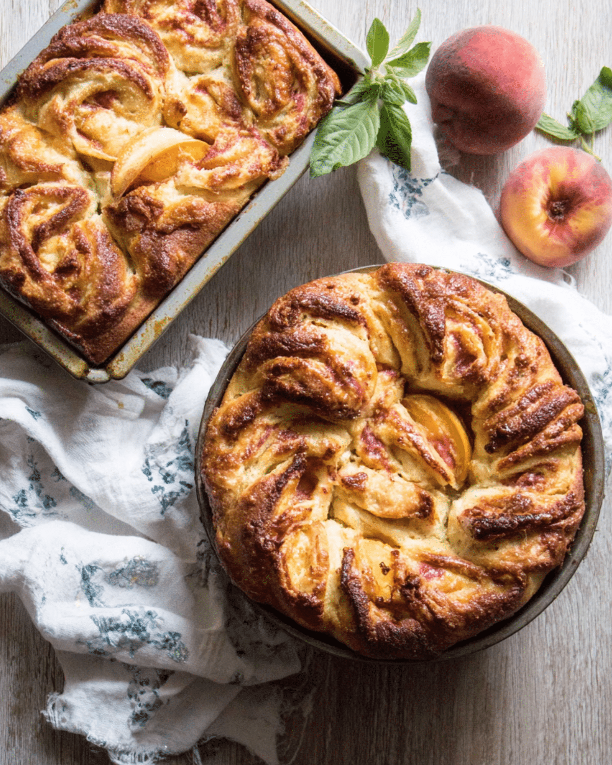Freshly baked Peach Brioche in round and loaf pans, featuring golden swirls of dough and slices of peaches nestled in the bread.