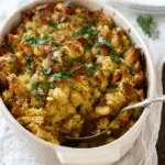 Perfect Homemade Stuffing in a white baking dish, golden and crispy on top, garnished with chopped fresh herbs.