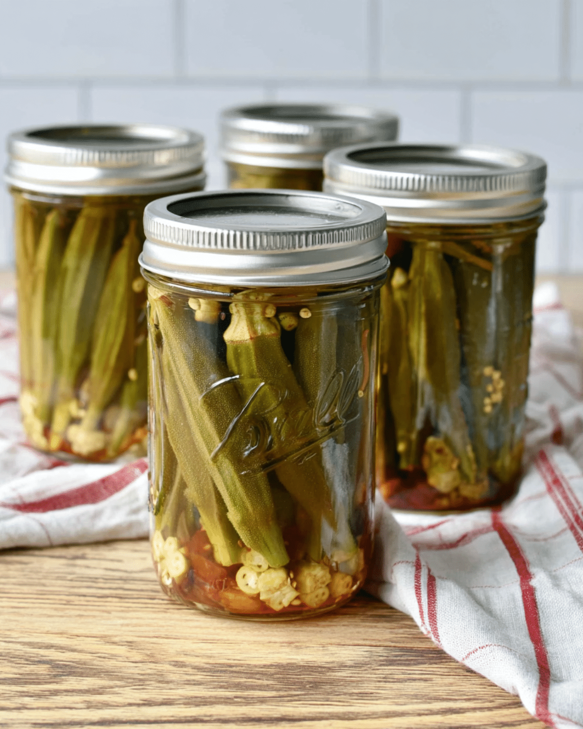 Jars of pickled okra sealed with metal lids, filled with whole okra, garlic, and spices on a wooden surface.