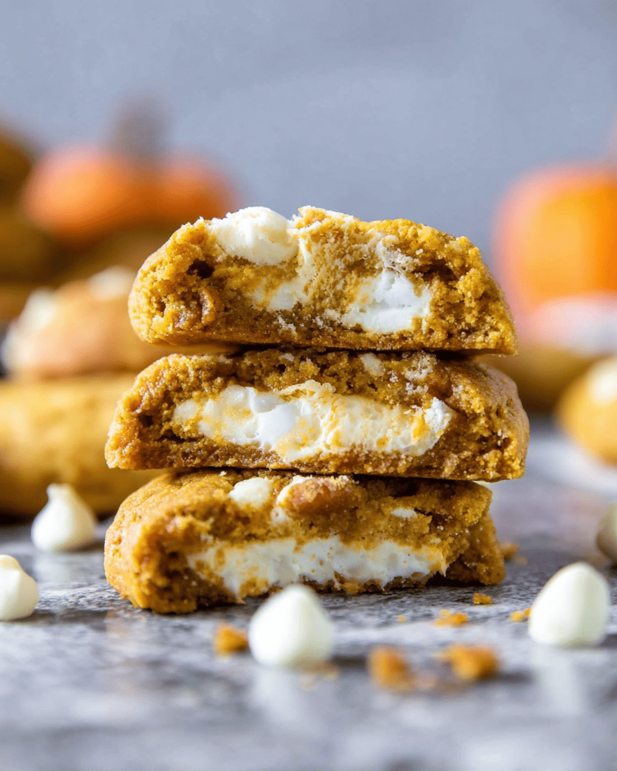 Stack of pumpkin cheesecake cookies with creamy cheesecake filling and white chocolate chips on a marble surface.