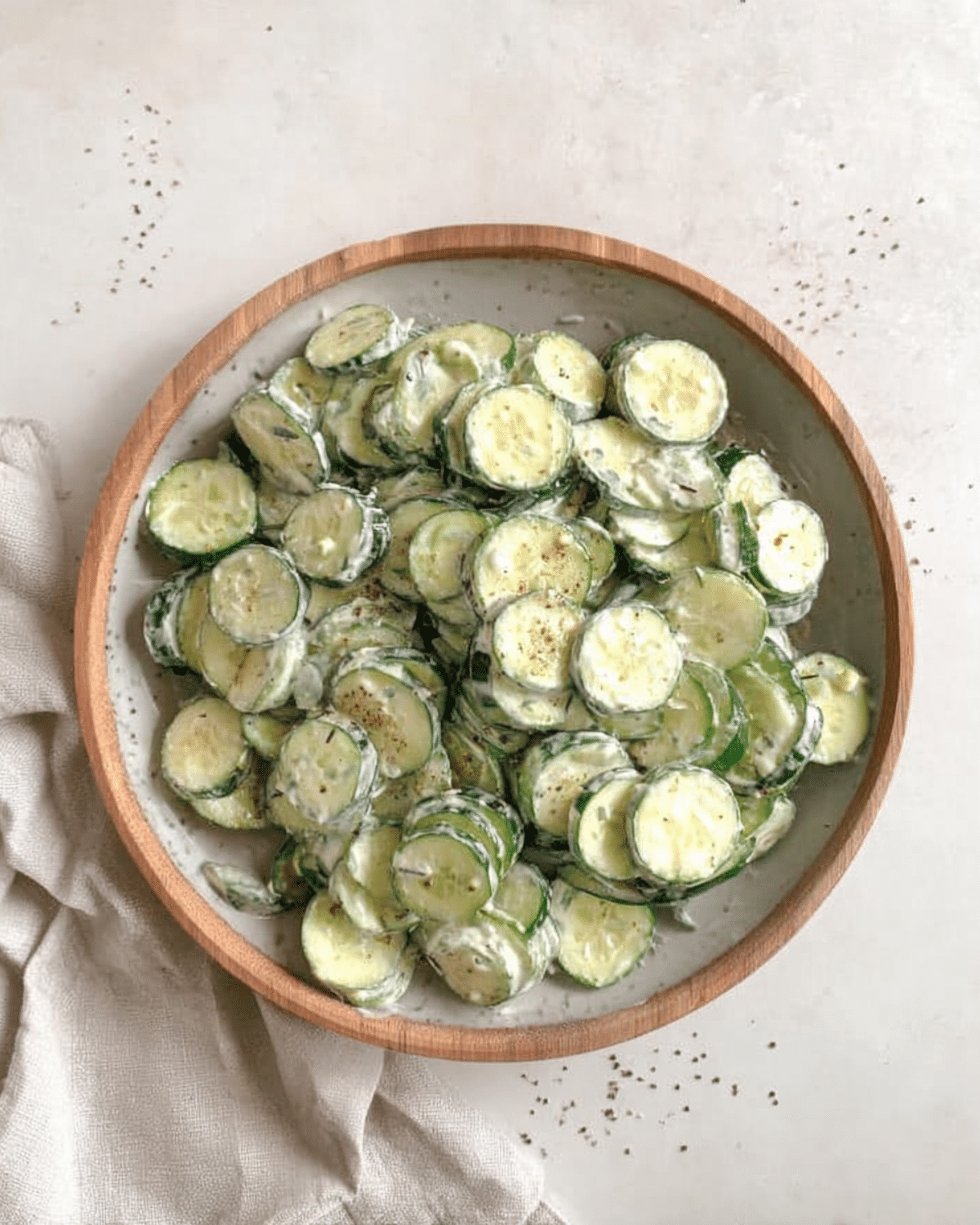 Wooden bowl filled with ranch cucumber salad featuring sliced cucumbers coated in a creamy ranch dressing and sprinkled with black pepper.