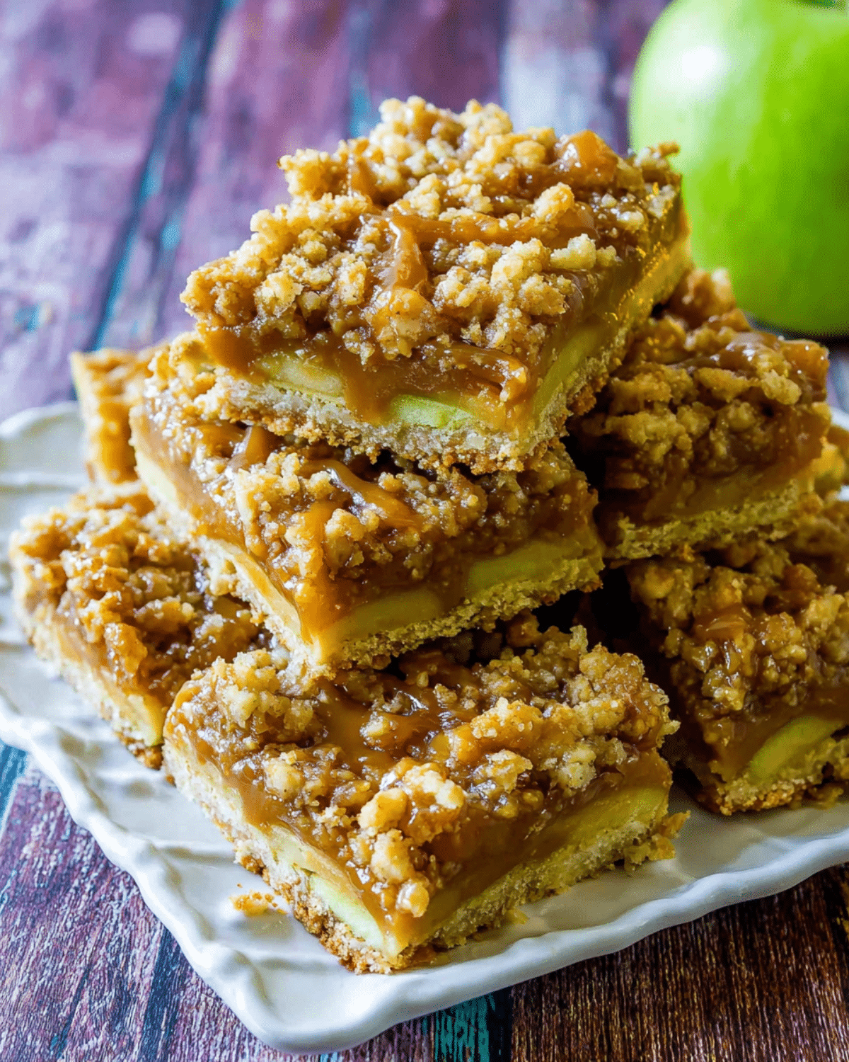 Salted Caramel Apple Bars stacked on a white plate, featuring layers of apples, caramel, and crumb topping.