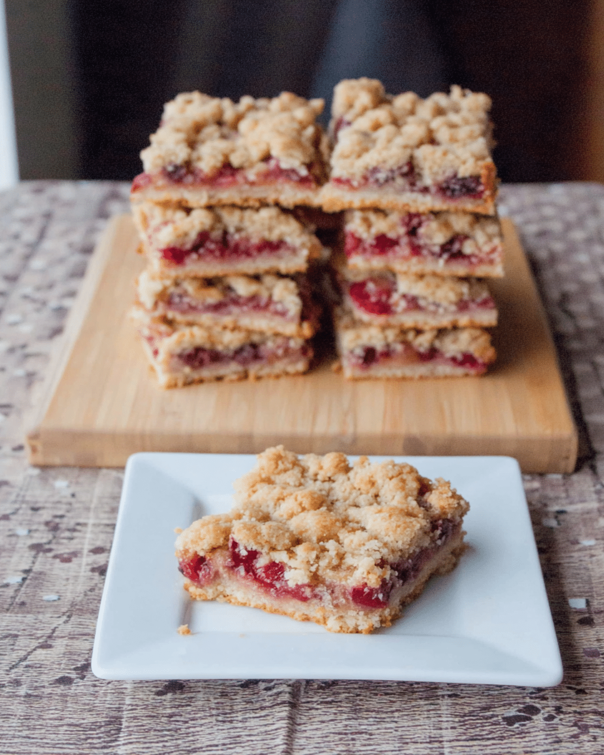 A stack of sour cherry crumble bars with one piece served on a white plate in the foreground.