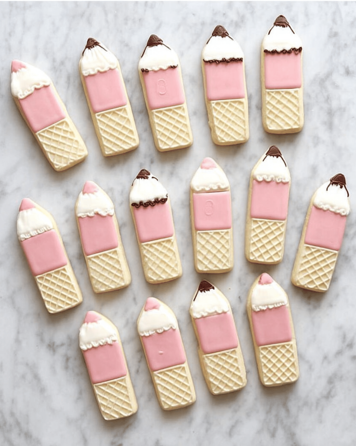 Wafer pencil cookies decorated with pink, white, and brown icing, arranged neatly on a marble surface.