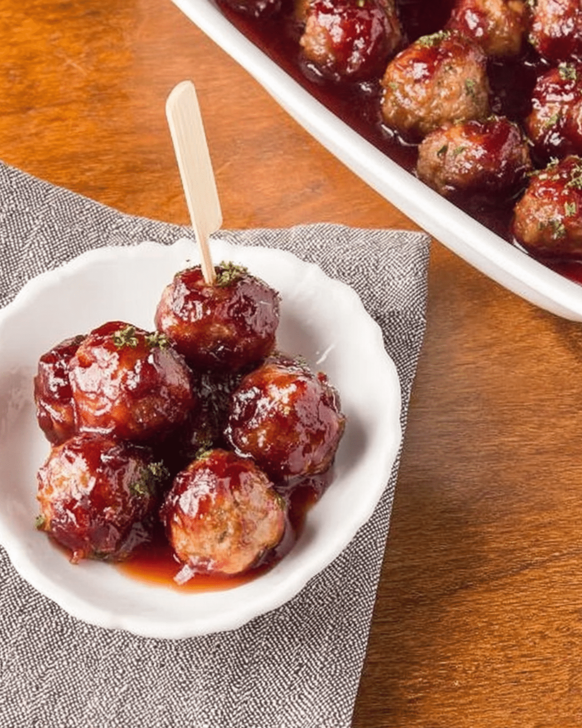 Best Christmas Cranberry Meatballs served in a small white dish with a toothpick, coated in a glossy cranberry sauce.