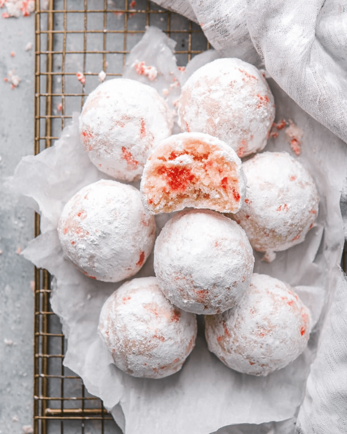 Cherry Snowball Cookies coated in powdered sugar, with one cookie bitten to reveal a pink cherry-filled center.