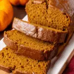 Homemade pumpkin bread sliced on a white platter with small pumpkins in the background.