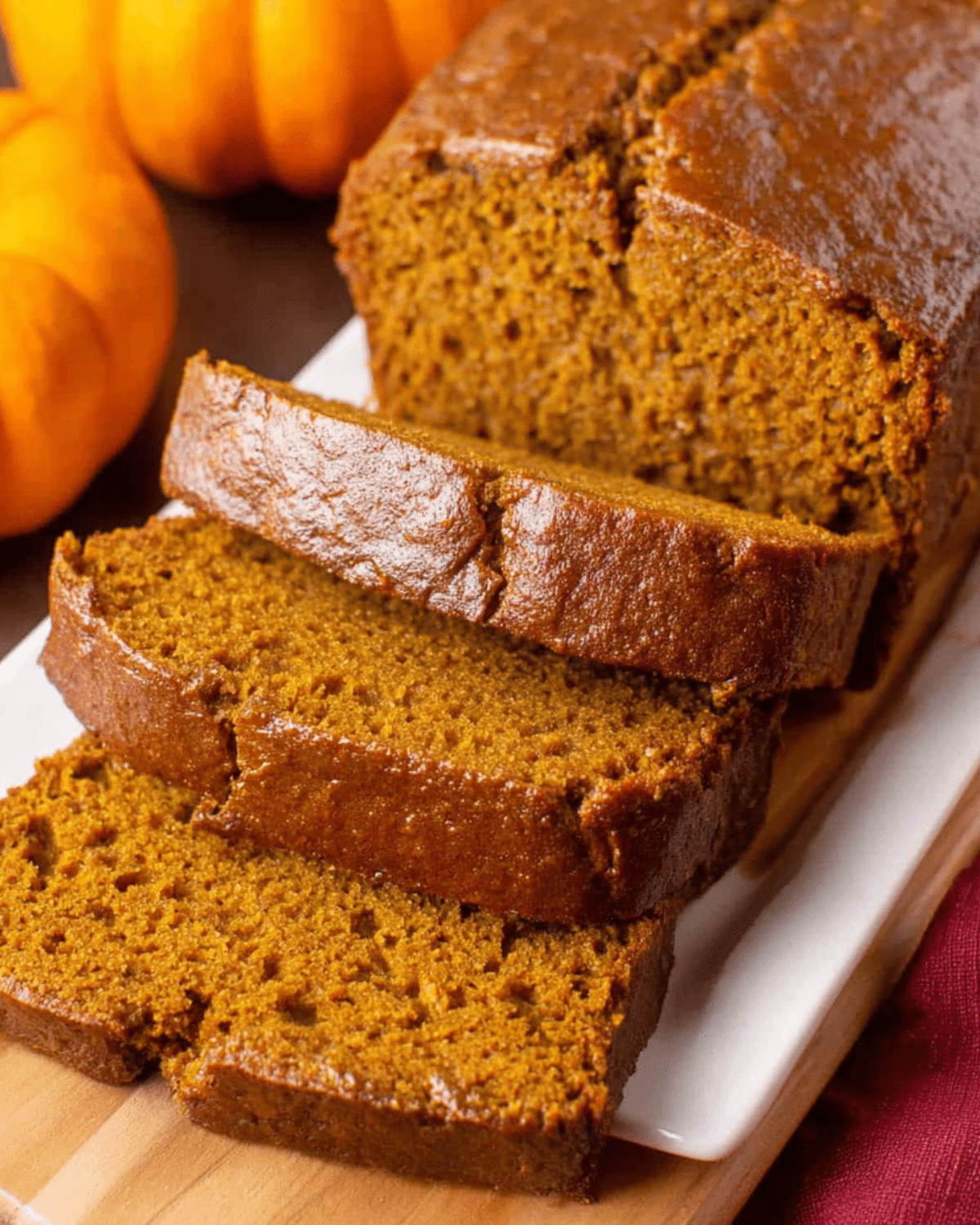 Homemade pumpkin bread sliced on a white platter with small pumpkins in the background.