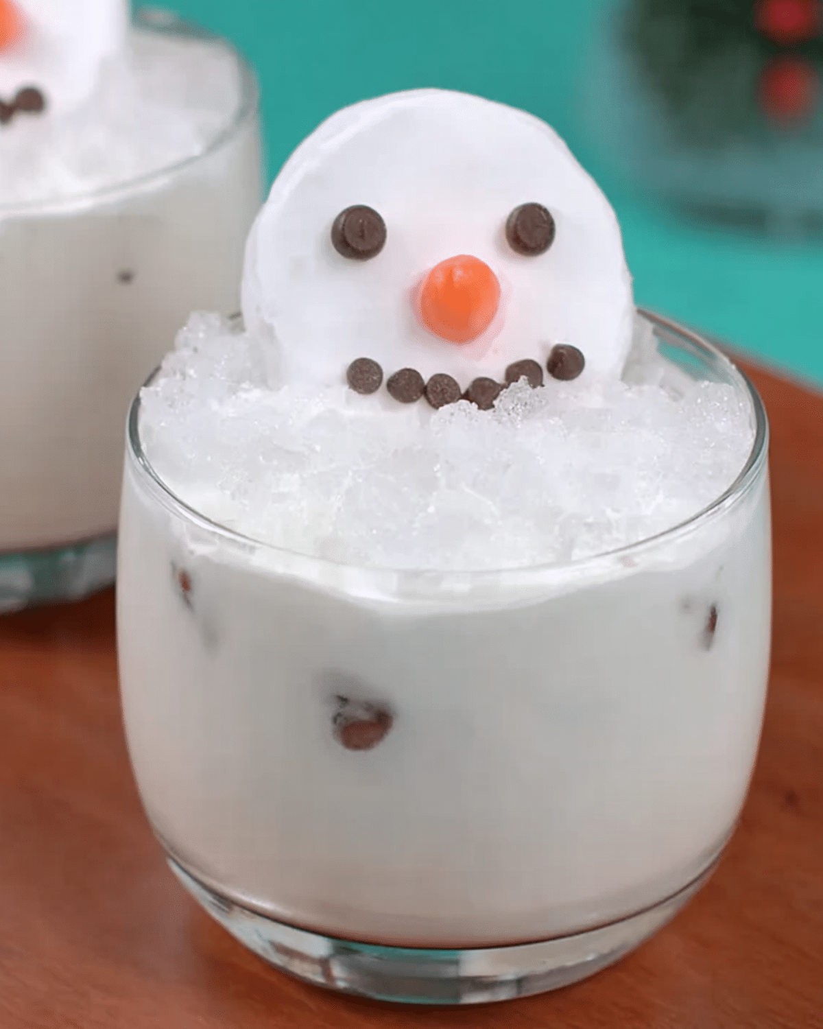 Melting Snowman Mocktail in a clear glass with ice, creamy white drink, and a marshmallow snowman face garnish.