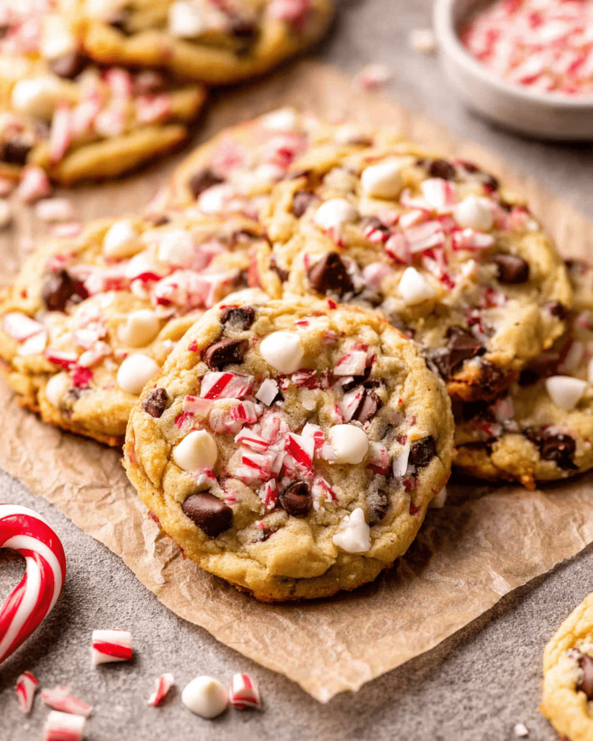 Peppermint Chocolate Chip Cookies topped with crushed candy canes, white chocolate chips, and dark chocolate chips on parchment paper.